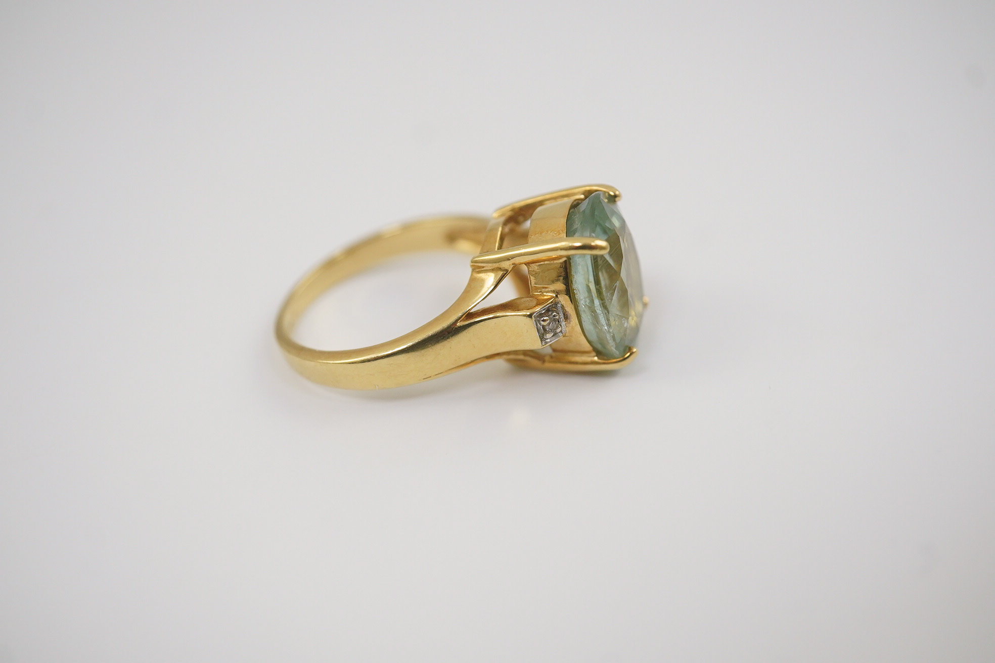 A modern 18ct gold and oval cut pale green tourmaline set dress ring, with two stone diamond chip set shoulders